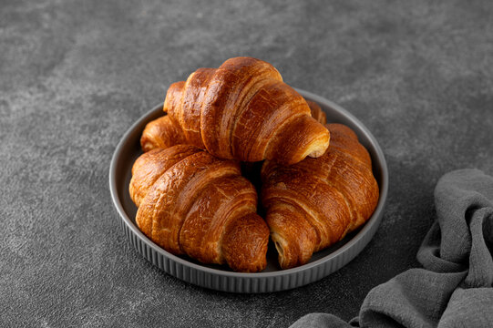 Fresh golden homemade croissants for breakfast on a gray plate on a dark concrete background.