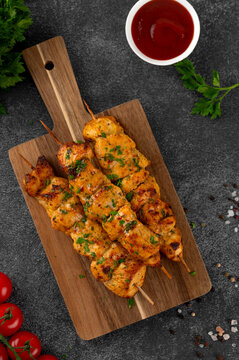 Juicy chicken skewers cooked in an air fryer and served on a wooden board with fresh herbs, cherry tomatoes and dipping sauce. Healthy food. Top view, copy space.