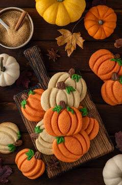 Themed dessert for Thanksgiving. Spiced cookies in the shape of white and orange pumpkins on a wooden board on a dark wooden background. Top view, copy space.