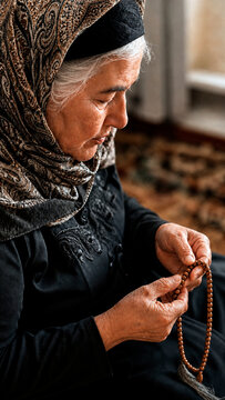 elderly Muslim woman holding wooden prayer beads. Senior female in a headscarf praying indoors with tasbih. Islamic faith and devotion concept