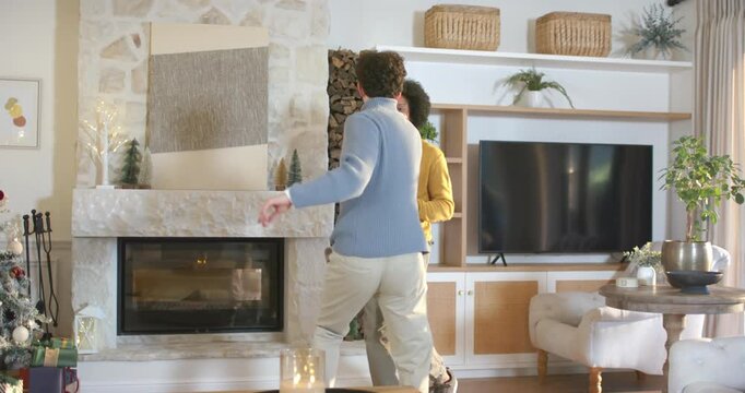 African American men holding hands, dancing twirling by stone fireplace, celebrating in sweaters