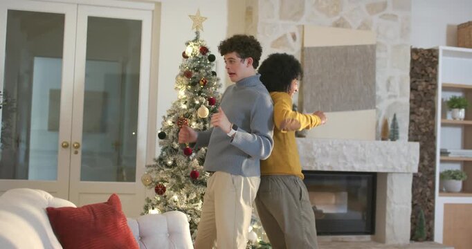 Two men standing back-to-back in living room by lit Christmas tree, moving then embracing joyfully