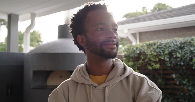 Sunlight shifting as man turning toward camera smiling on porch by oven wearing hoodie