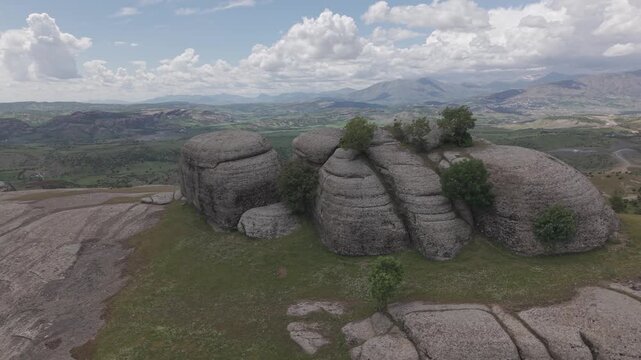 Smooth 4K 30fps aerial flight turns left beside a massive rock, passing close to unusual green trees growing on top. Shot in a flat color profile, ideal for color grading and LUT application.