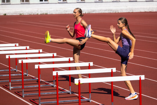 Adult and teenage female athletes lift legs over training hurdles. Concept of flexibility, dynamic stretching, coordination, high jump preparation and joint practice.