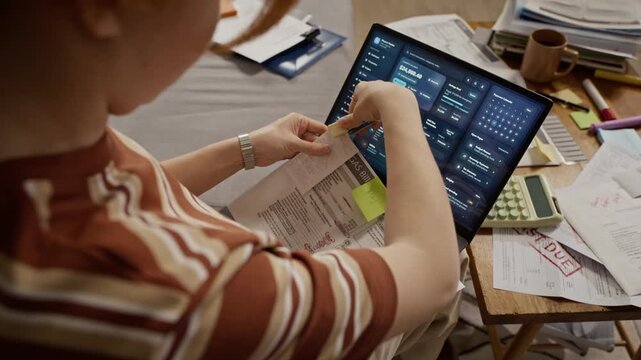Young adult Caucasian woman managing personal finance, holding gas bill and typing on laptop with financial dashboard. Footage represents home budgeting, debt management, and online banking