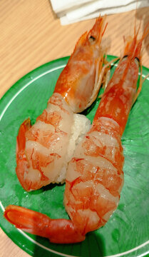 A vibrant piece of fresh raw shrimp sushi, featuring a sweet botan ebi served over tightly pressed vinegared rice and placed on a bright green ceramic plate.