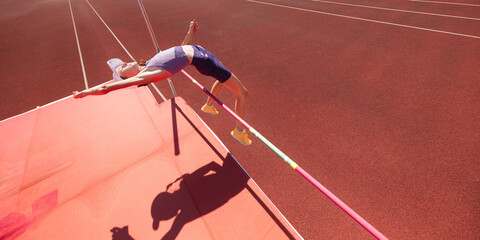 Fototapeta premium Teenage athlete clears high jump bar in overhead stadium view. Concept of youth sport, flight technique, agility, competition, achievement and athletic development.