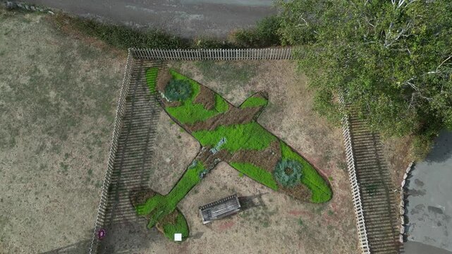 Paignton, Devon, England: DRONE VIEWS: A floral arrangement in the shape of a Spitfire in honour of RAF pilot, Flight Lt Frederick Denston. The surrounding grass has been burnt in the 2026 drought.