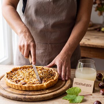 Frau schneidet Zwiebelkuchen neben Glas Federwei&szlig;er an
