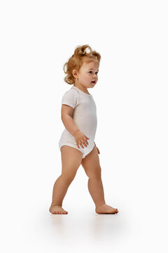 Toddler girl walking barefoot in white bodysuit. Concept of first steps, balance, coordination, independence, physical activity and healthy child development.