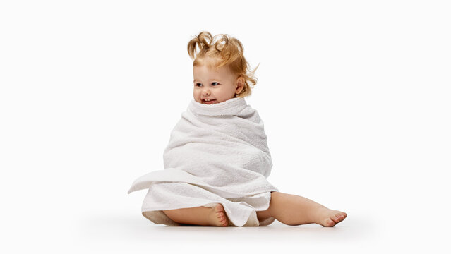 Toddler girl sitting wrapped snugly in white towel. Concept of post bath comfort, drying, hygiene and cozy self care, for parenting, healthcare and education.