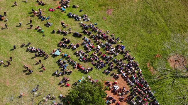 Camping Rally 2026 spectators gather beside the rally stage in Nueva Alborada, Itapua, Paraguay, South America, forming a large crowd along the rural course, top-down drone forward flyover.