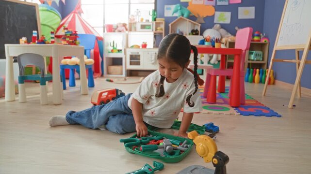 Girl holds toy screwdriver and plays with a toolkit while sitting on the floor in a building playroom; curiosity imagination focus.
