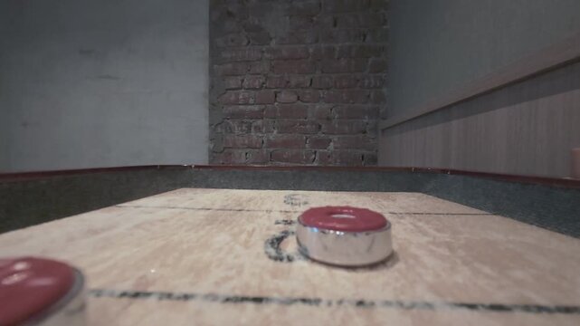 Two red shuffleboard pucks slide toward the camera and score