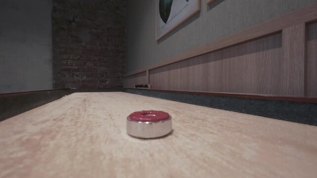 Close-up of a red shuffleboard puck resting on a waxed maple board