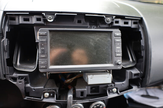 A car multimedia head unit with a touchscreen is installed in a partially disassembled center console. The process of removing or replacing the stereo displays internal mounts and dashboard components