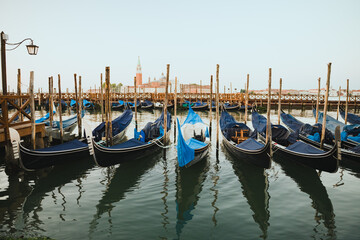 Traditional Venetian gondolas moored along the waterfront in Venice, Italy, creating a scenic view of historic boats, wooden poles and reflections on calm water. © Anastasia