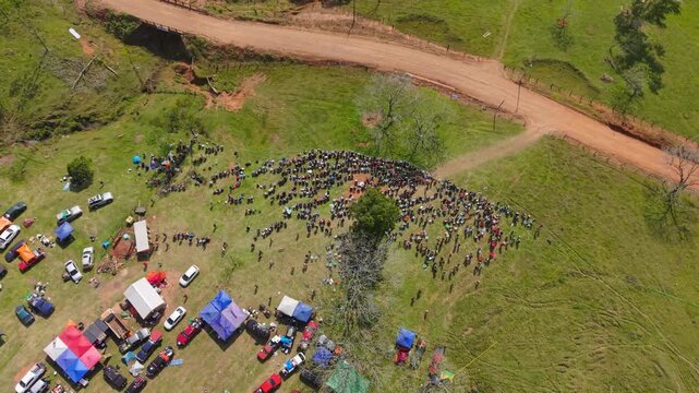 Drone video captures a vibrant crowd gathered on grassy hillsides with colorful tents and parked cars at the WRC Rally 2026 in Nueva Alborada, Paraguay, on a bright sunny day.