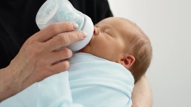 Mom Feeding Newborn Baby Boy With A Bottle While Rocking Him In Arms