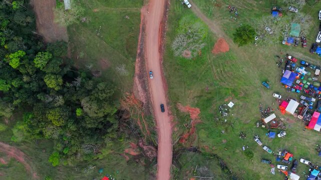 Drone video captures cars on a dirt track near lush Paraguayan forest and colorful pit tents, set before the WRC Rally 2026 event in Nueva Alborada.