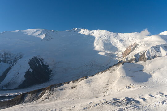 Snow-covered north face of Lenin Peak in morning light under clear blue sky, August shot from Kyrgyzstan side.