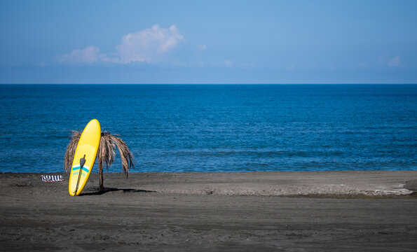 Yellow paddleboard on black sand beach by ocean