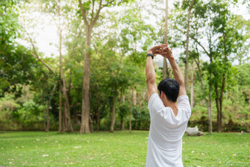 Obraz premium Asian man stretching arms overhead in green park for outdoor workout routine