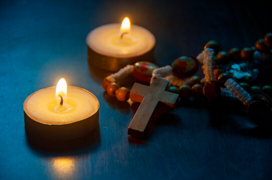 Lit candle with rosary beads and crucifix representing peaceful Christian prayer with customizable space for text.