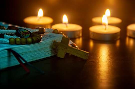 Open Bible with glowing candles and rosary beads representing Christian faith, devotion, and prayer with customizable space for text.