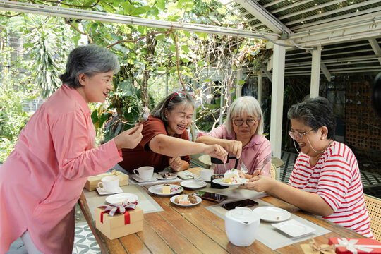 Older friends lean in to share cake at an outdoor cafe, smiling and laughing as they gather around the plate in a cheerful reunion filled with companionship and sweet shared delight, aging society.
