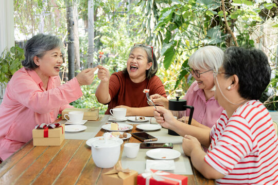 A group of friends talks over tea and cake at an outdoor cafe, sharing smiles and conversation during a relaxed reunion that celebrates companionship and warm meaningful time together, aging society.