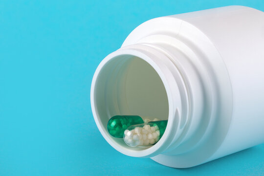 Close-up of green capsule and white pills in a white medicine bottle on a blue background, suitable for healthcare and pharmaceutical concepts.