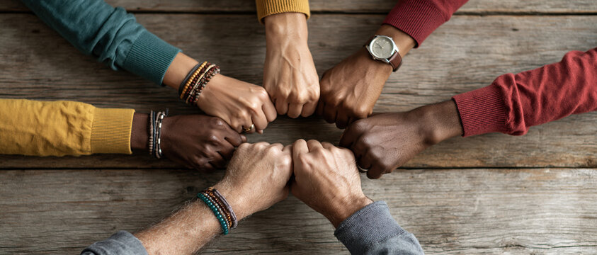 Overhead shot of eight diverse hands fistbumping in a circle over a rustic wooden table a powerful visual of inclusion, solidarity, and team spirit for campaigns celebrating unity.