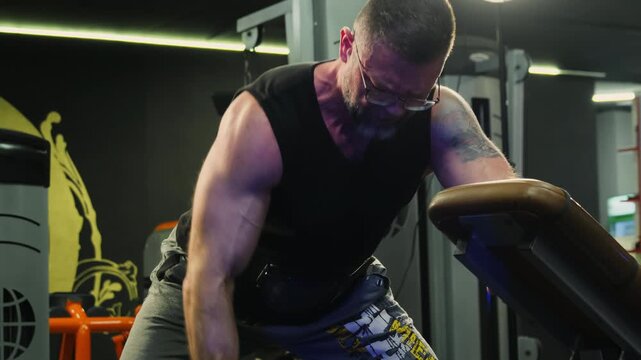 Man performs heavy one arm dumbbell row near padded bench. Athlete drives elbow backward engaging broad back muscles through strong effort
