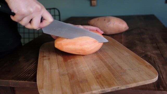 Close up of hands slicing a large sweet potato lengthwise on a wooden board