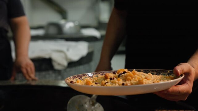 Uzbek oshpaz chef skillfully tosses freshly cooked plov while serving it onto a plate. Traditional Central Asian cuisine. Tourism, travel, gastronomy, cultural documentaries 
