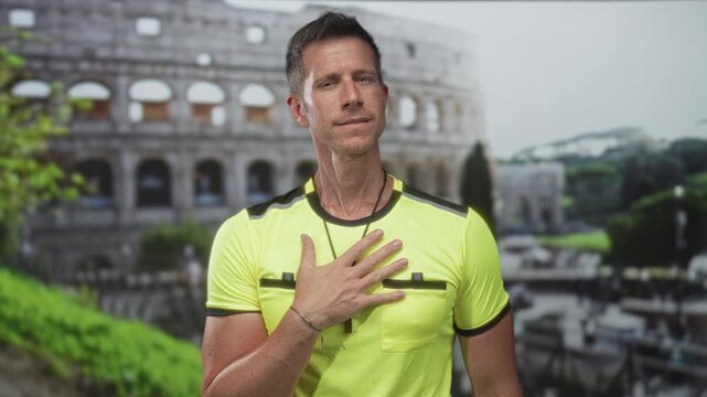 Man with hand pressed to chest in building by the coliseum wearing bright yellow shirt and whistle necklace; gratitude humility.