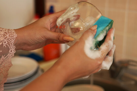 Young woman washing a glass with a soapy sponge, close-up of hands doing kitchen chores and housework stock photography