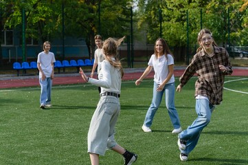 Obraz premium Group of teenage high school students play tag together on an outdoor school sports field during a break. Boys and girls chase each other, run and try to tag their classmates on artificial grass.