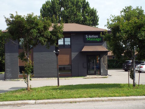 Gatineau, Quebec, Canada &ndash; July 02, 2026: An exterior street view of the dark gray commercial building housing "Solution Massage" with trees and a parking lot at 229 Boul. Saint-Ren&eacute; O.