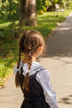 Schoolgirl in school uniform walking along park path from behind