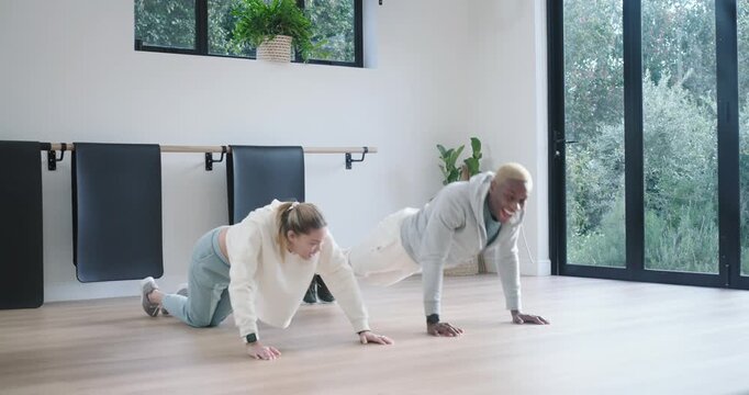 Diverse partners starting, doing push-ups by barre while man adding knee drives