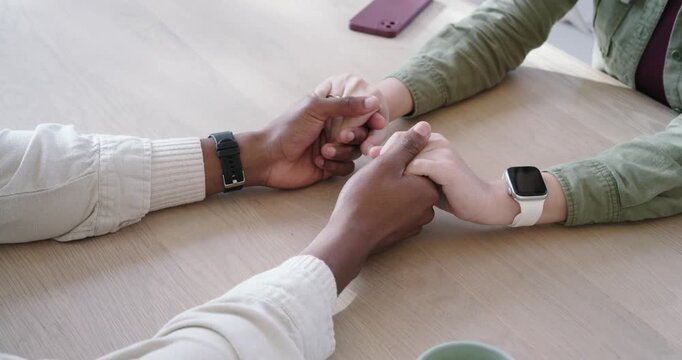 Left hand is shifting grip after rest, rubbing partner's fingers on table near mug for comfort