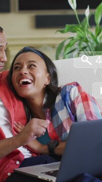 Animation of social media notifications over african american couple using laptop embracing on couch