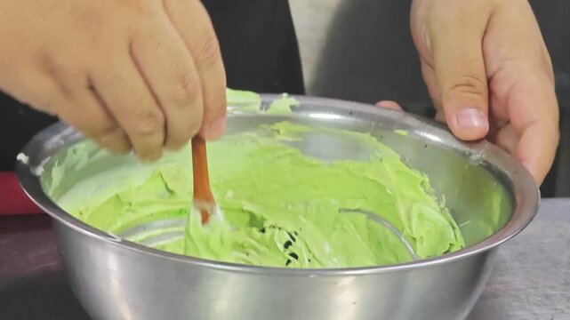 Adding liquid food coloring with a dropper into green cake cream.