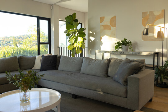 Gray L-shaped sectional sofa is anchoring living room near sunny window with round coffee table