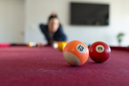 Female leaning over red-felt pool table aiming cue stick toward 13 ball in game room