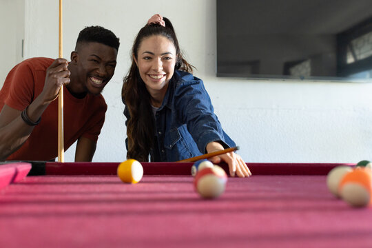 Asian woman and African American man playing pool in recreation room at magenta table holding cues