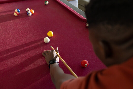 Man leaning over red-felt pool table at home aiming cue toward cue ball, balls, copy space